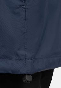 Gros plan sur l'ourlet d'une veste bleu marine avec un verrou de cordon noir réglable et des détails de couture.