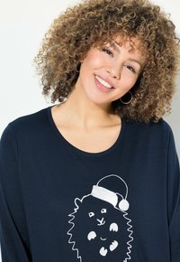 Maglietta a maniche lunghe blu navy con un design di un leone cartone animato che indossa un cappello di Babbo Natale. Tessuto morbido e liscio con scollatura rotonda.