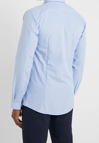 Chemise à manches longues bleu clair avec un design ajusté, des poignets boutonnés et des détails de dos yoke, fabriquée en tissu en coton lisse.