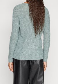 Mintgrön stickad tröja med en strukturerad söm, ribbade manschetter och nederkant. Bärs med högmidjade svarta läderbyxor.