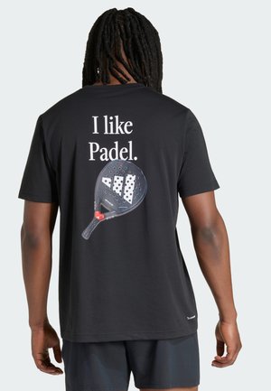 Muž s dredy, který má na sobě černé tričko s nápisem "Mám rád padel" a grafikou padelové rakety na zádech, zobrazen zezadu.