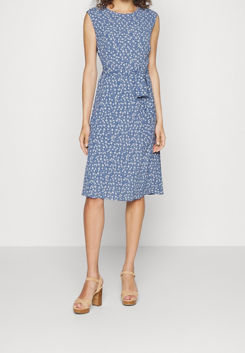 Modré květinové šaty s krátkými rukávy, úzkým pasem a sukní ke kolenům. Mají bílé květinové vzory na jednolitém pozadí.