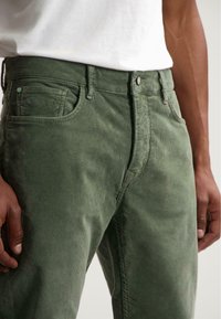 Pantalones de pana verde con una superficie texturizada, que cuentan con un cierre de botón, bolsillos frontales y un diseño de pierna recta.