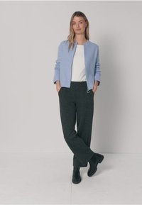 Jasnoniebieska krótka kurtka, biały top, ciemnoszare szerokie spodnie i czarne botki za kostkę. Spodnie mają detal z pętelką na zamek.