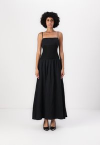 Μαύρο μέγιστο φόρεμα με εφαρμοστό κορσέ, λεπτές τιράντες και φουσκωτό, πλισέ φούστα. Λείος υφασμάτινος σκελετός και κλασικός σχεδιασμός. Συνοδεύεται από μαύρες γόβες.