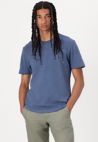 Blå kortermet henley-skjorte med tre knapper, laget av myk stoff, kombinert med lys grønn bukse. Enkel, uformell design.