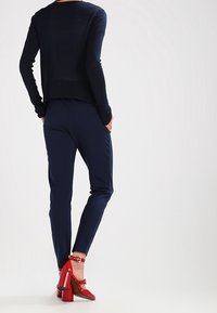 Navy long-sleeve top, fitted silhouette; paired with slim-fit navy pants. Bright red high-heeled shoes with ankle straps, glossy finish.