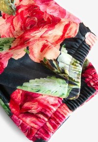 Blommönstrad tyg med stora rosa och röda rosor på en mörk bakgrund. Mjuk textur med detaljer i samlad elastisk midja.