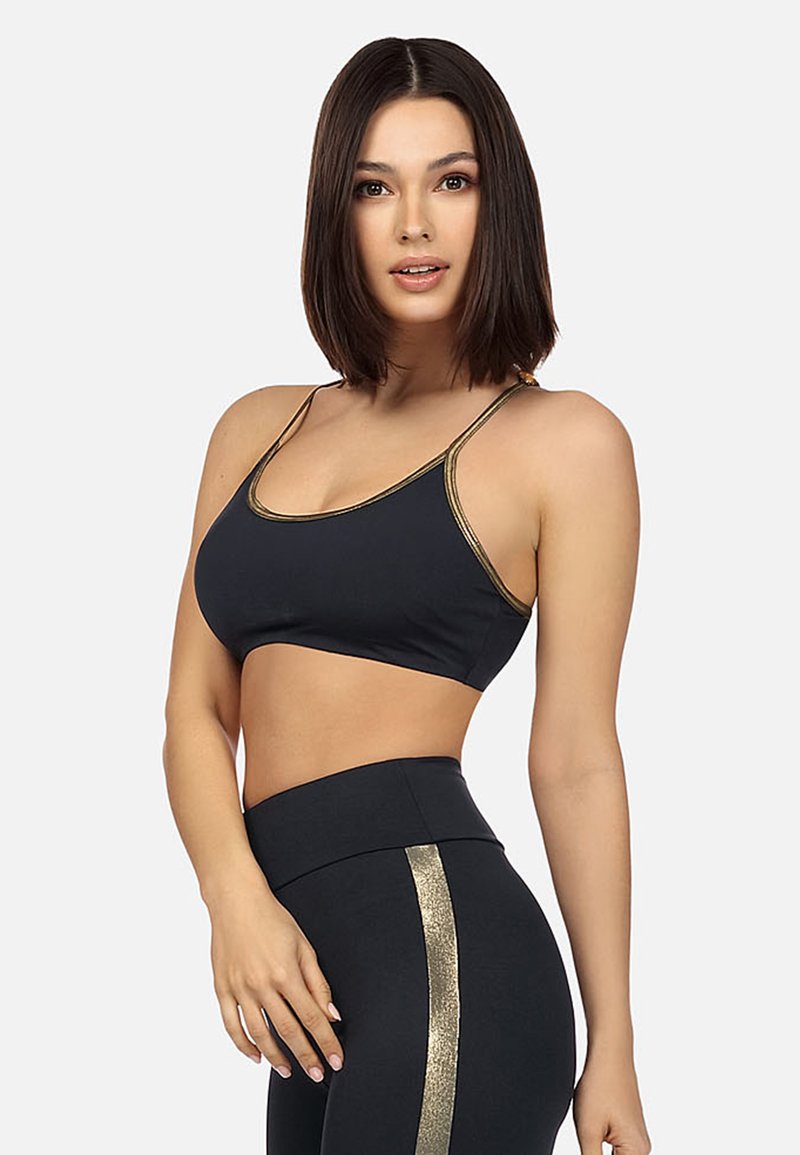 Czarny stanik sportowy z złotymi akcentami i cienkimi ramiączkami, w połączeniu z czarnymi legginsami w wysokim stanie z pionowym złotym paskiem.