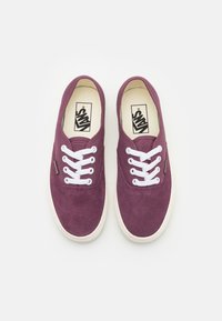 Pár fialových tenisek Vans s bílými tkaničkami a gumovými podrážkami pohledem z vrchu na bílém pozadí.