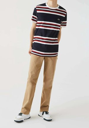 Marineblauw gestreept T-shirt met rode en witte banden, ronde hals. Gecombineerd met beige broek met rechte pijpen en witte sneakers met zwarte accenten.