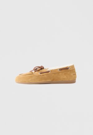 Pantofole mocassino in suede marrone con punta tondeggiante, dettaglio con lacci e una calda fodera bianca. Presenta una suola piatta in gomma per una buona aderenza.