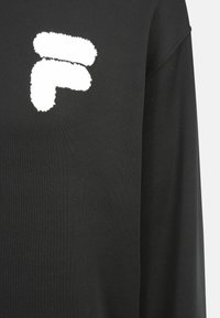 Czarna bluza z logo w białym kolorze o fakturowanej powierzchni umieszczonym po lewej stronie. Tkanina wygląda na gładką z lekko elastyczną fakturą.