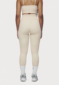 Beige sports bra and high-waisted leggings made of stretchy material. The leggings feature a smooth texture and fitted design, paired with white socks and grey sneakers.