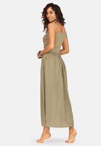 Maxi sukienka w oliwkowym kolorze ze sznurowanym topem, regulowanymi ramiączkami i zwiewnym dołem. Wykonana z lekkiego materiału o miękkiej strukturze.