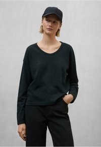 Čierne blúzka s dlhým rukávom z ľahkého materiálu s širokým výstrihom, spárovaná s čiernymi nohavicami a zodpovedajúcou čiapkou, vytvára monochromatický vzhľad.