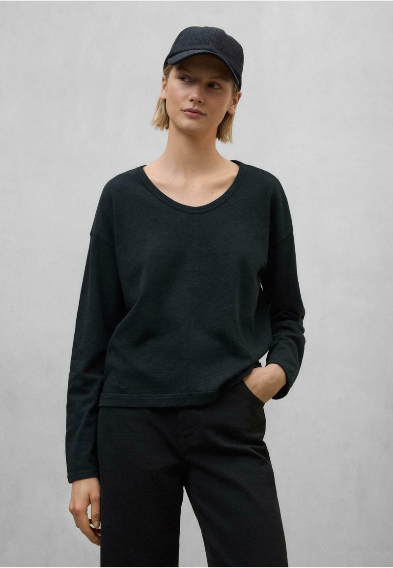 Čierne blúzka s dlhým rukávom z ľahkého materiálu s širokým výstrihom, spárovaná s čiernymi nohavicami a zodpovedajúcou čiapkou, vytvára monochromatický vzhľad.