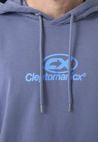 Grauer Hoodie mit langen Ärmeln und Kordelzug. Auf der Vorderseite prangt ein großes blaues Logo mit der Aufschrift "Cleptomanicx®". Weicher Stoff.
