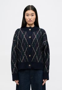 Cardigan tricot marine avec motif argyle en vert, violet et crème. Il dispose d'une fermeture à boutons, d'un col haut et d'une coupe décontractée.