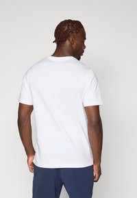 Hvid bomulds t-shirt med klassisk rund hals, korte ærmer og en komfortabel pasform,vist fra ryggen, med en glat overflade.