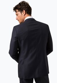Dunkelblaues Sakko mit taillierter Passform, glatter Textur und einem Schlitz auf der Rückseite. Der Kragen des weißen Hemdes ist sichtbar.