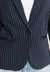 Navy bleiseri, jossa on pinstripe-kuviointi ja joustava kangas, avorivilla, yksittäinen nappisulku ja kaksi etutaskua.