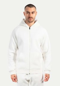 Vit zip-up hoodie i mjukt tyg; har en frontdragkedja, stor huva och kängurufickor med ribbad fåll och muddar.
