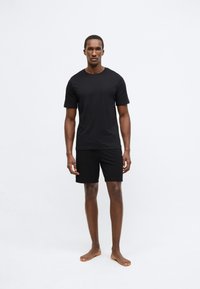 Μαύρο κοντομάνικο μπλουζάκι και αντίστοιχα σορτς από απαλό, λείο ύφασμα, με απλό, μοντέρνο σχέδιο χωρίς μοτίβα ή λογότυπα.