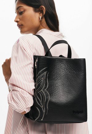 Zaino in pelle nera testurizzata con chiusura a zip, caratterizzato da cuciture decorative bianche in un motivo a foglia e logo sulla parte anteriore inferiore.