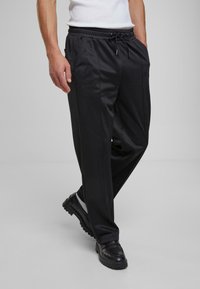 Sorte, letvægtsbukser med elastisk talje og snøre, der har sidelommer og en tapered ben-design. Glat tekstur.