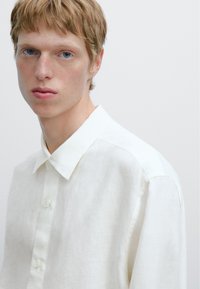 Witte linnen blouse met knopen en een klassieke kraag, zachte textuur en een subtiel geweven patroon. Eenvoudig ontwerp van de voorste knoopsluiting.