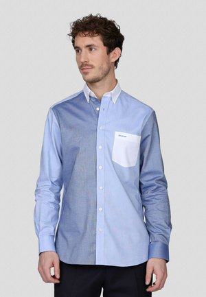 Chemise boutonnée bleu clair avec un panneau contrastant bleu foncé, poche blanche et un tissu lisse et texturé. Coupe ajustée avec des poignets boutonnés.