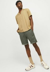 Chemise à boutons beige à manches courtes avec un col, associée à un short vert. Baskets blanches avec des accents rouges et chaussettes beiges montant jusqu'aux chevilles.