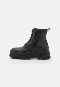 Bottines en cuir noir avec une semelle épaisse, un laçage à l'avant, un col rembourré et une tirette. Dotées d'œillets métalliques et d'accents texturés.