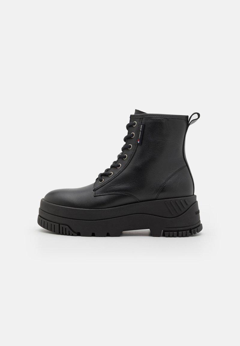 Bottines en cuir noir avec une semelle épaisse, un laçage à l'avant, un col rembourré et une tirette. Dotées d'œillets métalliques et d'accents texturés.