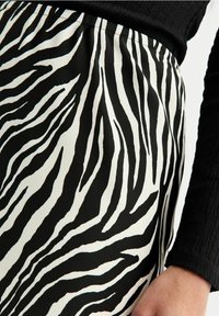 Sukně se zebřím vzorem v černobílé barvě vyrobená z hladké látky, s vysokým pasem a jemným leskem. Viditelný detail textury látky.