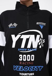 Black and white zip-up sweatshirt with racing graphics, including "YTN," checkered flag accents, and blue, red text elements.