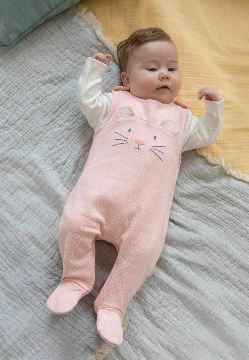 Rosa Baby-Overall mit Punkten und einem Hasengesicht-Design, aus weichem Stoff, mit langen Ärmeln und Füßen, auf strukturierten Decken ausgelegt.