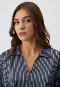 Blusa a righe navy con linee verticali in lavanda e bianco, con un colletto e una texture liscia e lucida.
