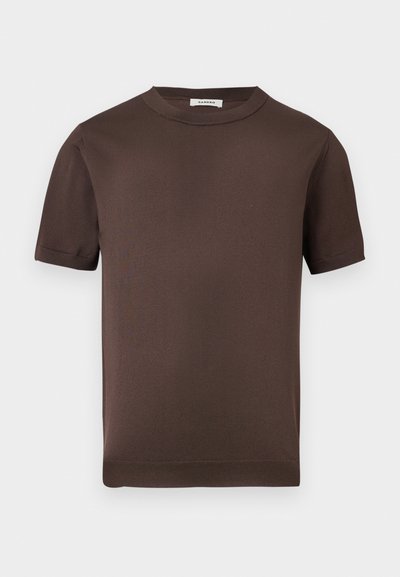 Καφέ κοντομάνικο πλεκτό μπλουζάκι με στρογγυλή λαιμόκοψη, ριμπ λαιμό και μανσέτες, απεικονισμένο σε απλό ανοιχτό γκρι φόντο.