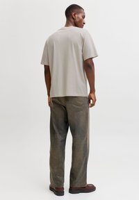 Ανοιχτό γκρι κοντομάνικο μπλουζάκι συνδυασμένο με χαλαρά εφαρμοστά χακί παντελόνια, με κλασικό κόψιμο και μίνιμαλ σχεδιασμό. Ορατά καφέ παπούτσια.