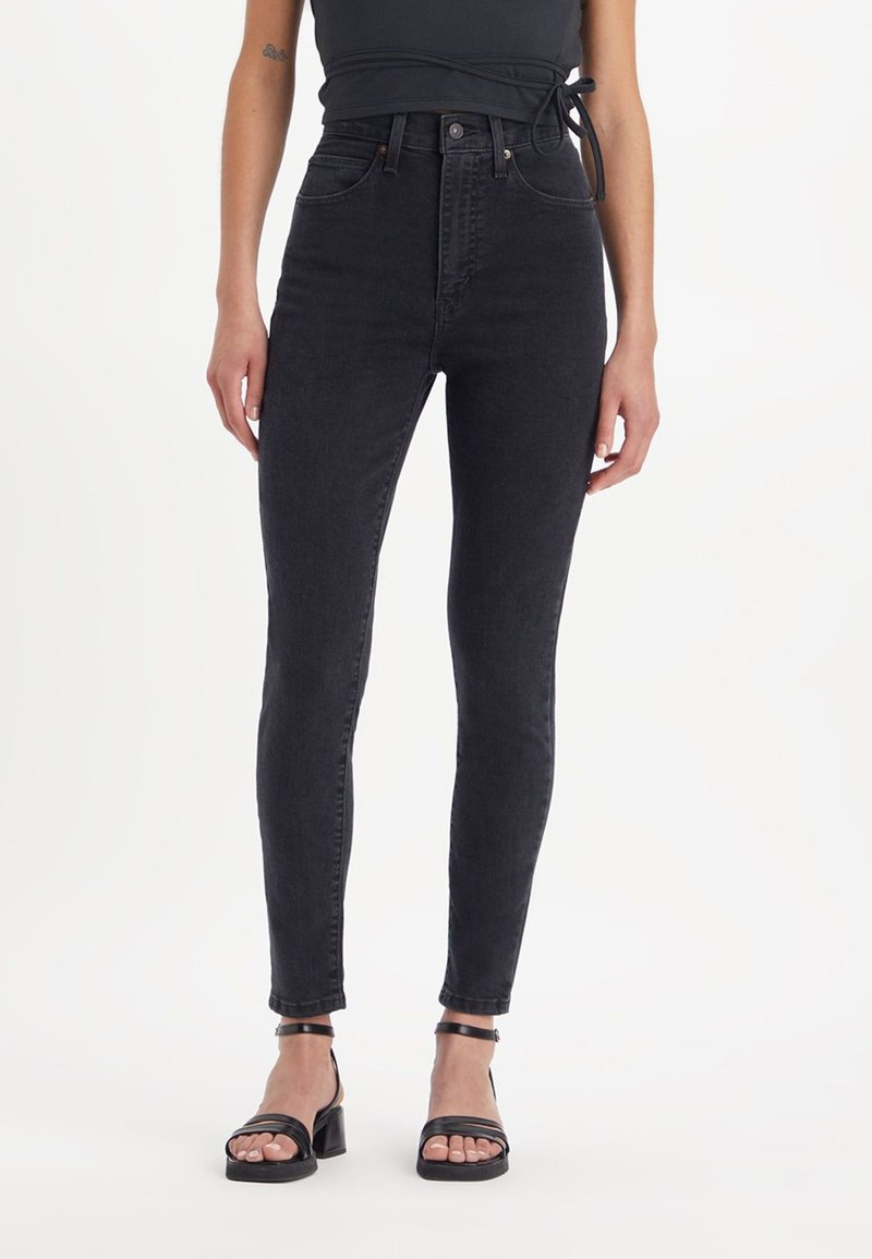 Høye svart jeans med smal passform, laget av denim. Har et frontlukking med knapp, klassisk fem-lomme design, og subtil søm.