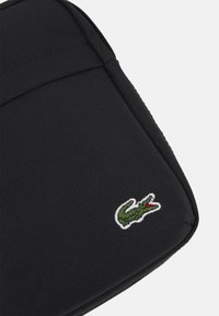 Černá pouzdro na laptop s texturovanou látkou, na dolním pravém rohu s vyšitým malým zeleným krokodýlem.