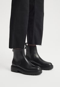 Czarne skórzane botki za kostkę z pionowymi żebrami, zaokrąglonym noskiem i grubą gumową podeszwą, w połączeniu z czarnymi krótki spodniami.