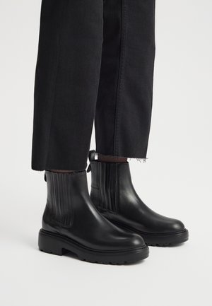 Czarne skórzane botki za kostkę z pionowymi żebrami, zaokrąglonym noskiem i grubą gumową podeszwą, w połączeniu z czarnymi krótki spodniami.