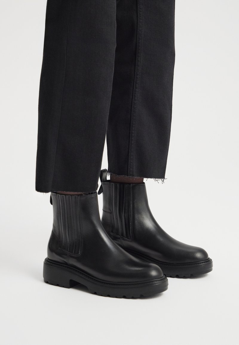 Czarne skórzane botki za kostkę z pionowymi żebrami, zaokrąglonym noskiem i grubą gumową podeszwą, w połączeniu z czarnymi krótki spodniami.