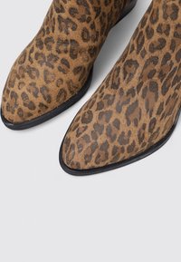 Bottines à imprimé léopard en daim marron avec un bout pointu et une semelle en caoutchouc noir. Présente un motif texturé sur le dessus.