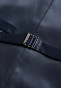 Marineblaues Satinmaterial mit glatter Textur, das mit einem metallischen Schnallenriemen verziert ist. Der Stoff hat einen leichten Glanz und ist tailliert.