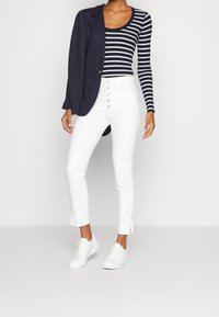 Marinblå blazer över en långärmad topp med svartvita ränder, i kombination med vita högmidjade skinny jeans och vita sneakers.