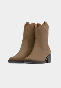 Ζευγάρι μεσαίου ύψους καφέ σουέντ καουμπόικες μπότες με διακριτικές ραφές, χρυστό φερμουάρ στη εσωτερική πλευρά και στιβαρούς τετράγωνους τακούνια.